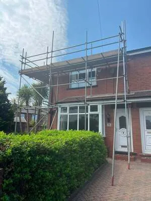 Scaffolding on a semi-detached house behind a garden hedge