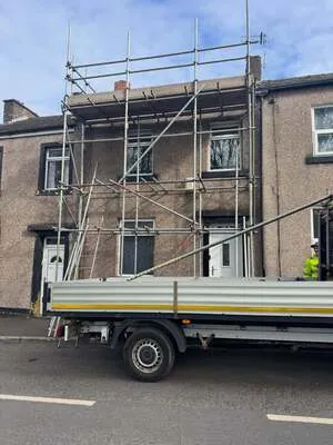 Scaffolding on a stone-fronted terraced house with a flatbed lorry outside