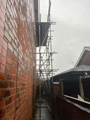 Scaffolding in a narrow passage beside a brick house